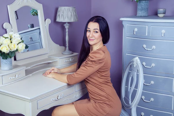Kahverengi elbise ve uzun siyah saçları onun odasına partiden önce poz onun tuvalet Masası yakınındaki güzel kadınla.