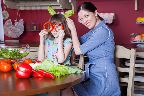 Happy mother and daughter enjoy making and having healthy meal together at their kitchen. they are making vegetable salad and having fun together. mom take care of her daughter and tech how to cook.