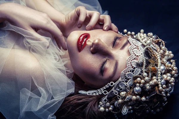 Fashion beauty portrait of young beautiful young woman with makeup and freckles on her face and pearl headpiece on her head and white tulle in front of her face on dark blue background. — Stock Photo, Image