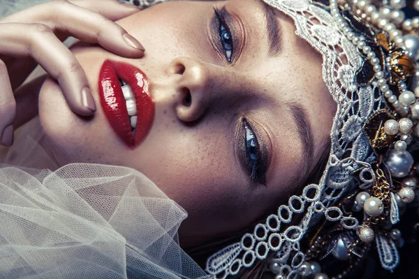 Moda beleza retrato de jovem bela mulher com maquiagem e sardas em seu rosto e headpiece pérola em sua cabeça e tule branco na frente de seu rosto no fundo azul escuro . — Fotografia de Stock