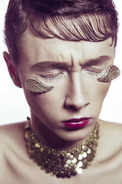 Yüksek moda güzellik altın genç modelinin delici takı ve makyaj kanatlar. Stüdyo vurdu.