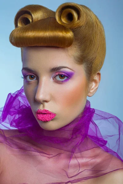 Colored fashion beauty woman with pink tulle and candy colored pearls on her lips and fantasy golden hairstyle on blue background. — Stock Photo, Image