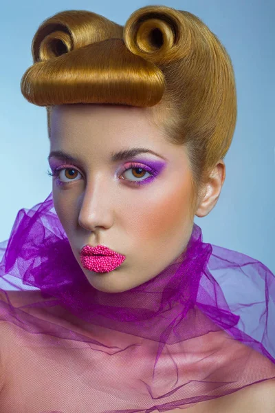 Mulher de beleza de moda colorida com tule rosa e doces pérolas coloridas em seus lábios e fantasia penteado dourado no fundo azul . — Fotografia de Stock