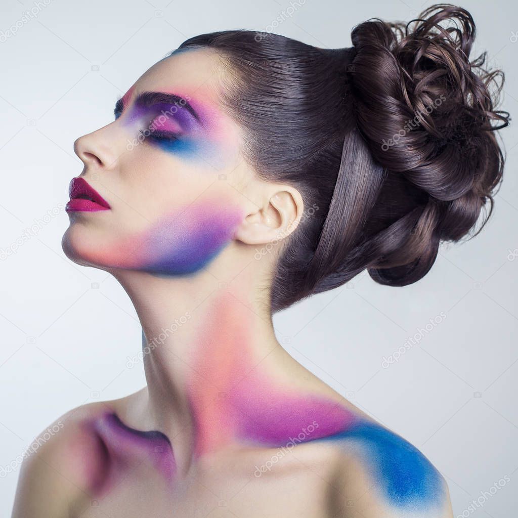 beautiful young woman with creative colored makeup and curly collected hairstyle and painted colored body. 