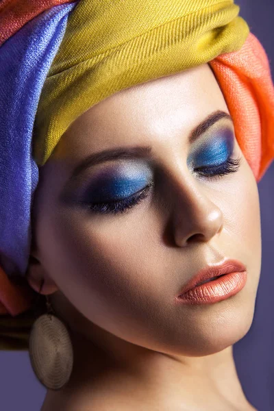 Schöne Frau mit farbiger Kopfbedeckung und blauem Make-up. — Stockfoto