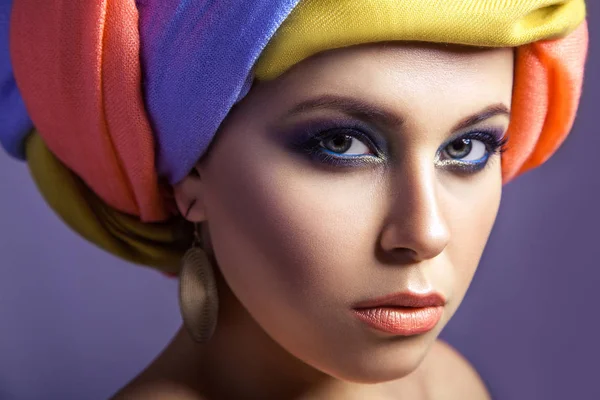 Schöne Frau mit farbiger Kopfbedeckung und blauem Make-up. — Stockfoto