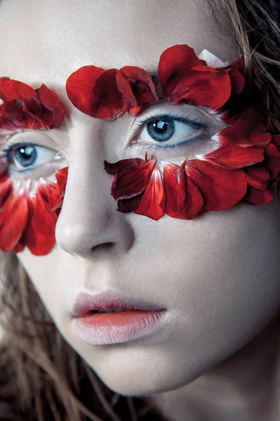 Retrato de belleza de la joven modelo de moda con pelos húmedos y pétalos de flores rojas alrededor de sus ojos. estudio de tiro sobre fondo azul —  Fotos de Stock