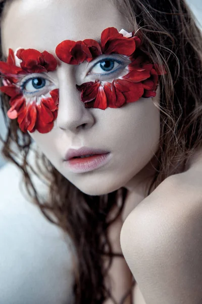 Retrato de belleza de la joven modelo de moda con pelos húmedos y pétalos de flores rojas alrededor de sus ojos. estudio de tiro sobre fondo azul —  Fotos de Stock