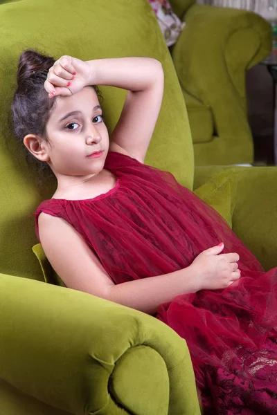 Carino amorevolmente ragazza del medio oriente con abito rosso scuro e capelli raccolti posa e sdraiati sul divano verde all'interno di casa. studio girato — Foto Stock