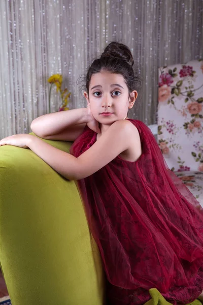 Menina bonito lovlely Oriente Médio com vestido vermelho escuro e cabelo recolhido posando e deitado no sofá verde em casa interior. estúdio tiro — Fotografia de Stock
