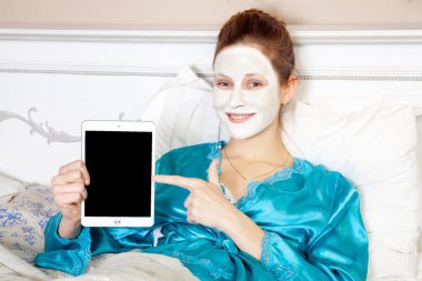 Güzel ve kadın ile yeşil gece yatağında dinleniyor ve uyumadan önce tablet holding beyaz yüz maskesi
