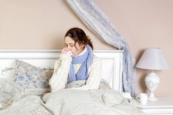 Flu. Gambar close-up dari frustrasi wanita sakit tergeletak di tempat tidur dengan syal biru tebal memegang tisu oleh hidungnya . — Stok Foto