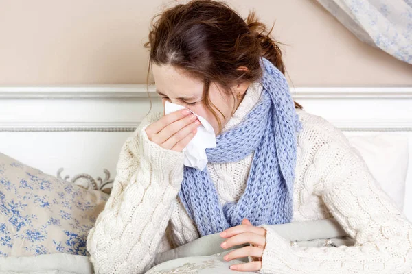 Förkyld. Närbild bild av unga sjuk kvinna blåser hennes näsa medan du sitter på sängen. — Stockfoto