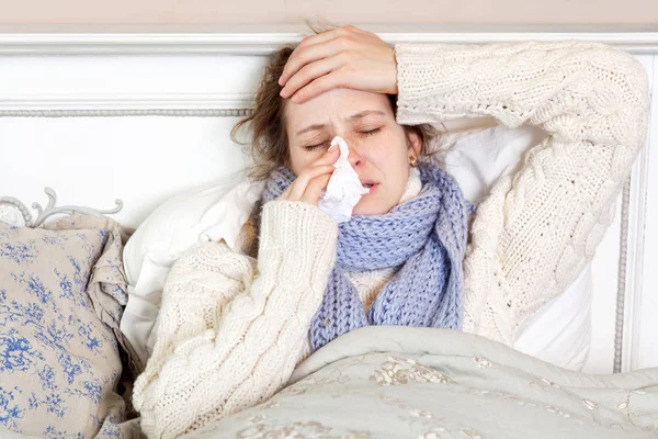 Flu. Gambar close-up dari frustrasi wanita sakit berbaring di tempat tidur dengan syal biru tebal memegang tisu oleh hidungnya dan menyentuh kepalanya dengan mata tertutup . — Stok Foto
