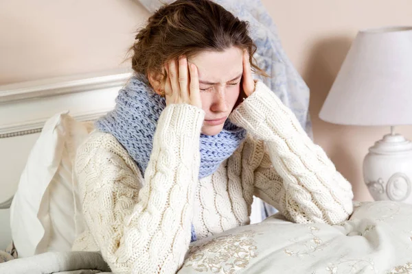 Grypa lub przeziębienie. Zbliżenie góry obraz sfrustrowany młoda kobieta z niebieski szalik i cierpi straszny ból głowy podczas leżenia w łóżku. — Zdjęcie stockowe