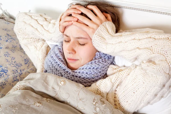 Gripe o frío. Vista superior de la imagen de la joven frustrada con bufanda azul y que sufre de dolor de cabeza terrible mientras está acostado en la cama . —  Fotos de Stock