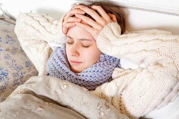 Gripe ou frio. Close-up vista superior imagem de mulher jovem frustrada com lenço azul e sofrendo de dor de cabeça terrível enquanto deitado na cama . — Fotografia de Stock