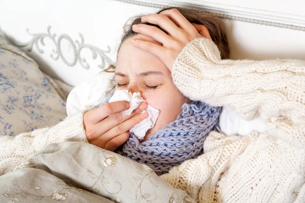 Influenza. Immagine da primo piano di una donna malata frustrata sdraiata a letto con una sciarpa blu spessa che le tiene il tessuto per il naso e le tocca la testa e le soffia il naso con gli occhi chiusi . — Foto Stock