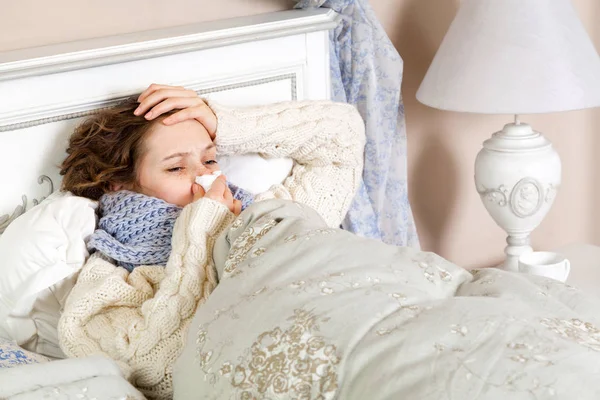 Flu. frustrasi sakit wanita berbaring di tempat tidur di syal biru tebal memegang jaringan oleh hidungnya dan menyentuh kepalanya . — Stok Foto