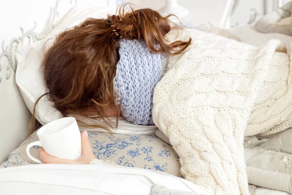 Wanita sakit dengan secangkir teh. Citra closeup dari wanita muda yang frustrasi sakit dalam syal biru rajutan memegang secangkir teh sambil berbaring di tempat tidur . — Stok Foto