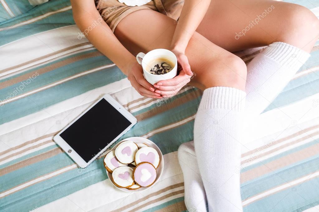 Soft photo of woman on the bed with tablet and cup of coffee.