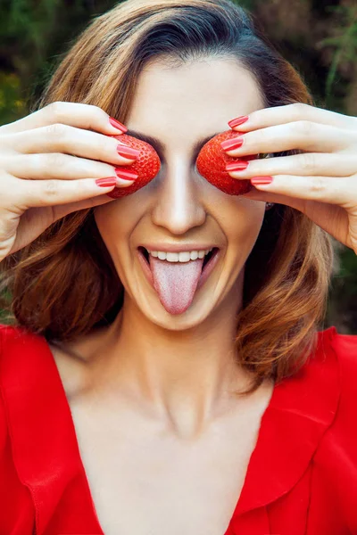 Menina engraçada feliz bonita nova com vestido vermelho e maquiagem segurando morango no verão no parque. estilo de vida saudável, dieta beleza e felicidade conceito . — Fotografia de Stock