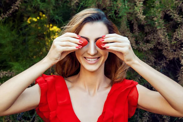 Joven hermosa chica divertida feliz con vestido rojo y maquillaje celebración de fresa en verano en el parque. estilo de vida saludable, belleza dieta y concepto de felicidad . —  Fotos de Stock