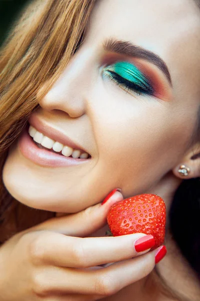 Junge schöne fröhliche lustige Mädchen mit rotem Kleid und Make-up hält Erdbeere im Sommer im Park. gesunder Lebensstil, Diätschönheit und Glückskonzept. — Stockfoto