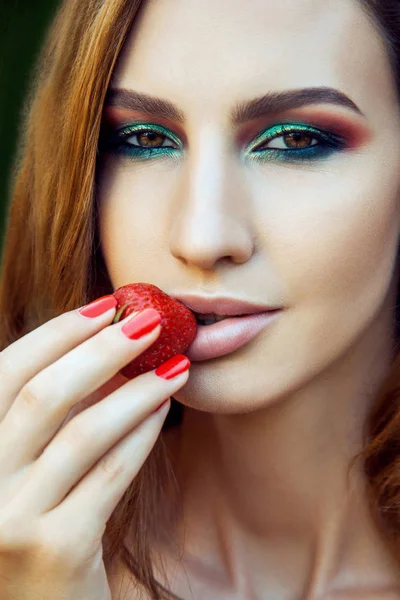 Junge schöne fröhliche lustige Mädchen mit rotem Kleid und Make-up hält Erdbeere im Sommer im Park. gesunder Lebensstil, Diätschönheit und Glückskonzept. — Stockfoto