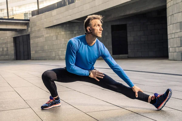 Stiliga atlet mannen i svart blå sport uniform stretching kropp — Stockfoto