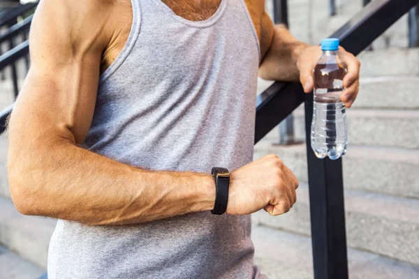 Спортсмен с бутылкой воды отдыхает и проверяет свои умные часы после бега. фитнес, спорт, физические упражнения и здоровый образ жизни людей . — стоковое фото
