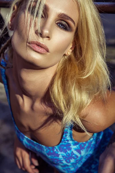 Όμορφη μόδας μοντέλο με γαλάζιο κορμάκι θέτοντας στις μεταλλικές σκάλες κοντά στην παραλία, σε ηλιόλουστες μέρες του καλοκαιριού. — Φωτογραφία Αρχείου