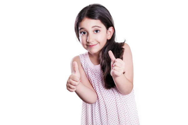 Linda menina feliz com cabelos longos e escuros e vestido olhando para a câmera com os polegares para cima. estúdio tiro, isolado em fundo branco . — Fotografia de Stock