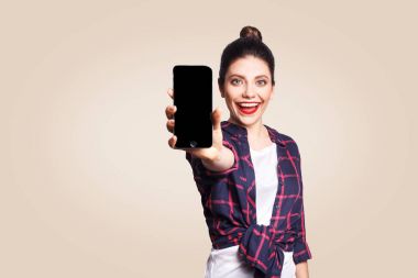 Kameraya bakarak ve telefonun ekranına gösterilen telefon tutarak rahat tarzı genç güzel kadın. bej renkli arka plan üzerinde atış stüdyo.