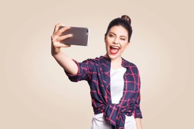 Telefon tutarak ve selfie akıllı telefon ile yapıyor rahat tarzı genç güzel mutlu kadın. bej renkli arka plan üzerinde atış stüdyo.