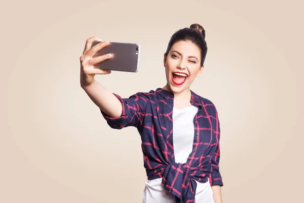 Joven hermosa mujer feliz en estilo casual sosteniendo el teléfono y haciendo selfie con el teléfono inteligente. estudio rodaje sobre fondo beige . — Foto de Stock