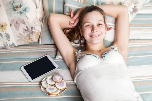 Retrato de mujer feliz con dulces y tabletas acostada en su cama . — Foto de Stock
