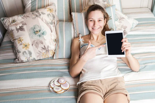 Portrait of happy woman with sweets and tablet lying down on her bed. — Stock Photo, Image