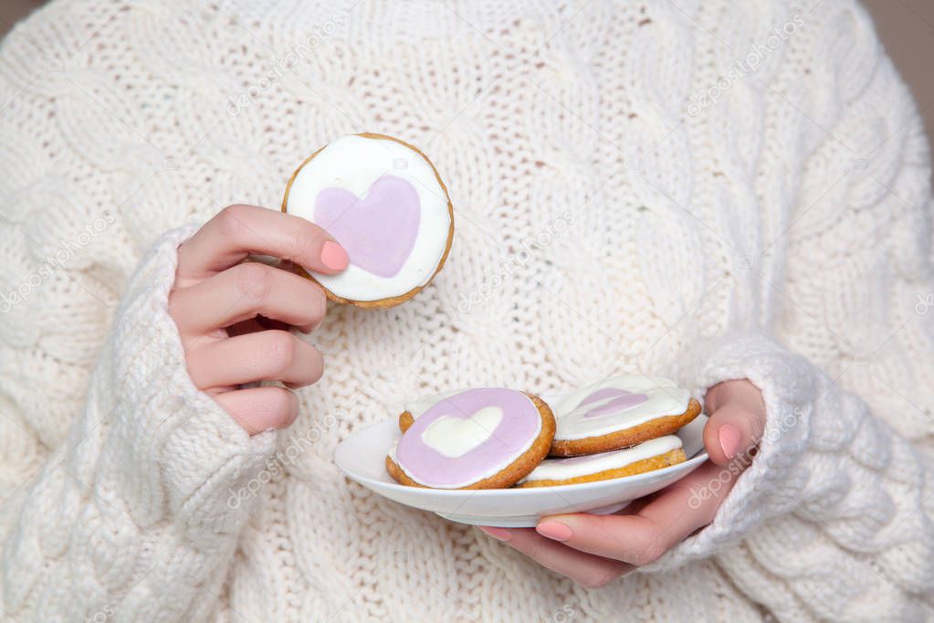 Closeup of woman with white sweater holding biscuit. 