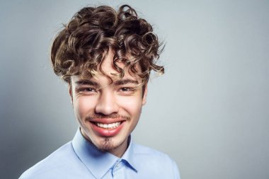 Kıvırcık saç modeli ile genç adam portresi. Stüdyo vurdu. Dişlek gülümseyerek kameraya bakıyor. 
