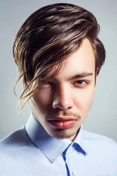 Portrait of young man with long fringe hairstyle on his eyes. studio shot. looking at camera. — Stock Photo, Image