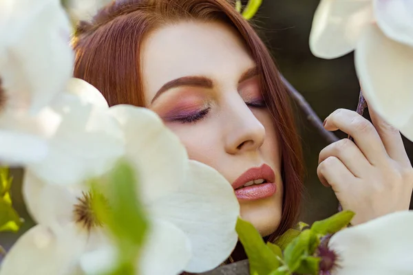 Retrato de una joven mujer hermosa posando entre árboles florecientes con sombra de ojos rosa . —  Fotos de Stock