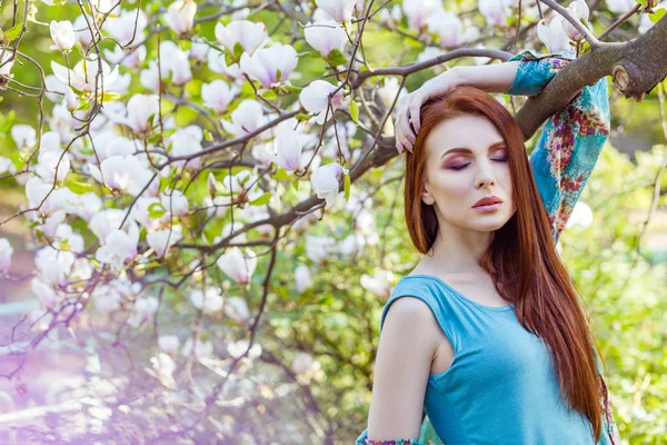 Retrato de una joven mujer hermosa posando entre árboles florecientes con sombra de ojos rosa . — Foto de Stock