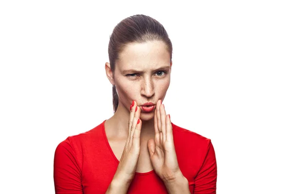 Retrato de una mujer seria en camiseta roja con pecas. mirando a la cámara y contando secretos, filmado en el estudio. aislado sobre fondo blanco . —  Fotos de Stock