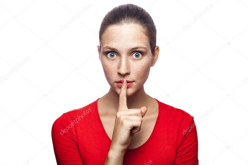 Portrait of serious woman in red t-shirt with freckles with shh sign on her lips. studio shot. isolated on white background. 