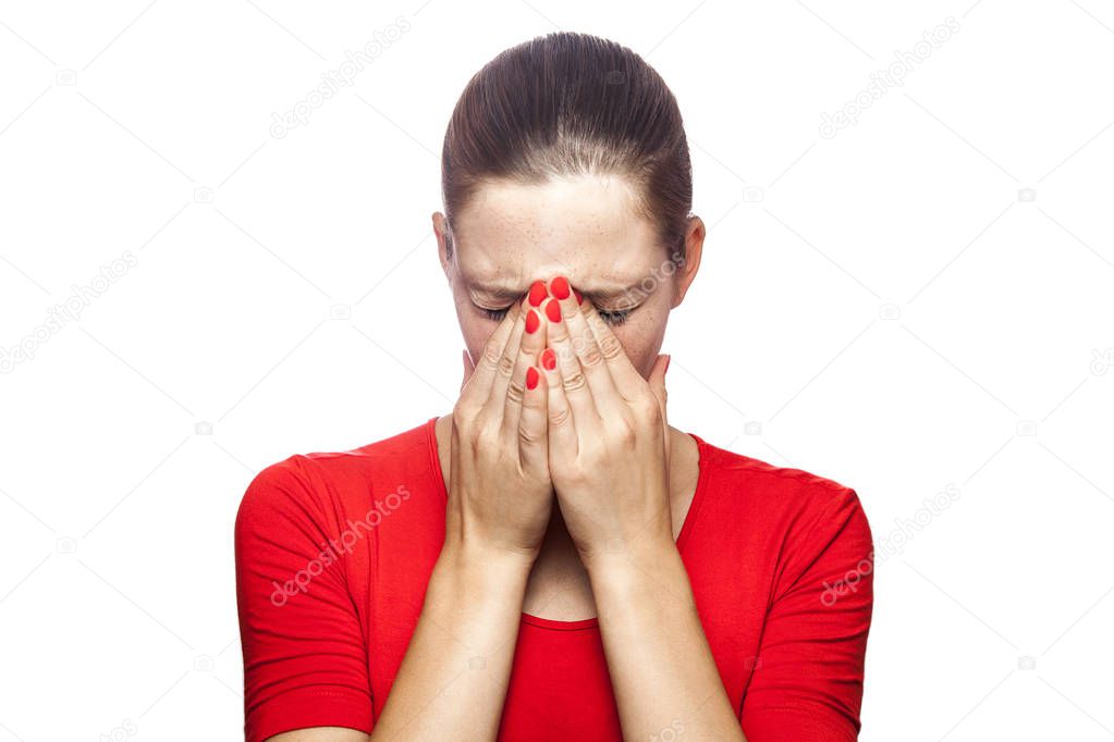 Portrait of sad unhappy crying woman in red t-shirt with freckles. closed eyes with hands, studio shot. isolated on white background. 
