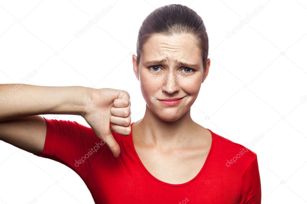 Portrait of unhappy sad woman in red t-shirt with freckles with finger down. looking at camera, studio shot. isolated on white background. 