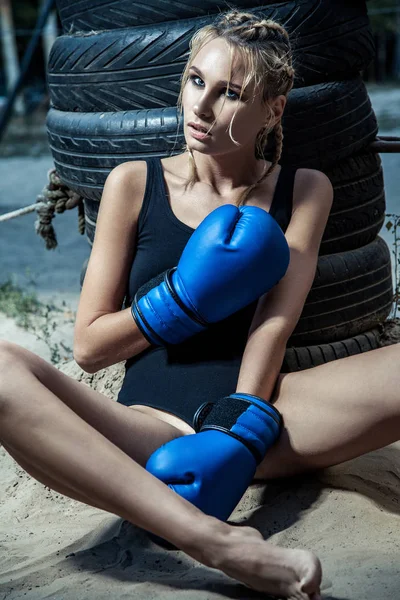 Fashion boxer woman in a black sportswear and with blue boxing gloves. outdoor workout of young blonde woman.