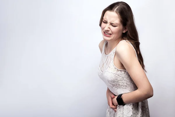 Retrato de mujer hermosa con pecas y vestido blanco y reloj inteligente con dolor de estómago sobre fondo gris plateado. concepto de salud y medicina . — Foto de Stock