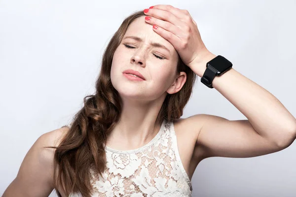 Porträtt av vacker kvinna med fräknar och vit klänning och smart Watch-klocka med huvudvärk smärta på silver grå bakgrund. vård och medicin koncept. — Stockfoto